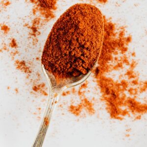 Top view of metal spoon with ground paprika in metal round bowl on marble desktop